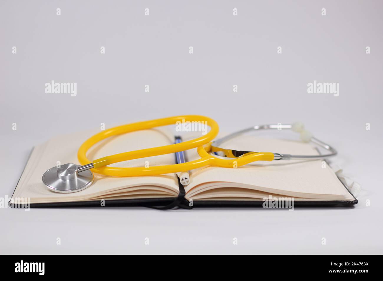 Uno stetoscopio medico con un cuore giallo su un notebook aperto con una penna blu per concetto medico Foto Stock