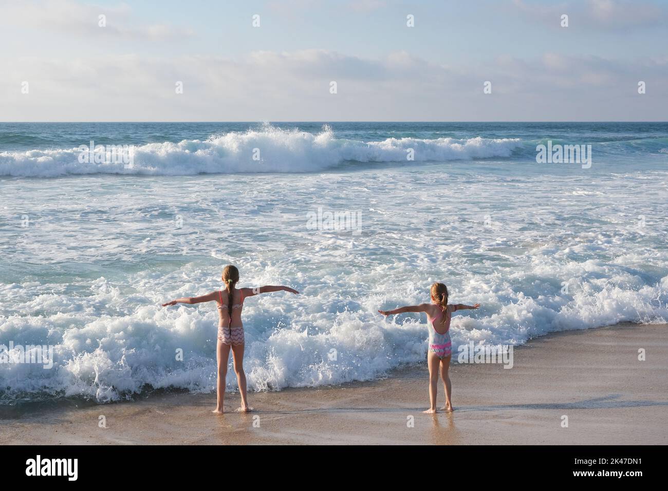 Due bambine piccole e graziose in piedi davanti all'oceano Atlantico con le mani aperte. I bambini giocano sulla spiaggia dell'oceano. Foto Stock