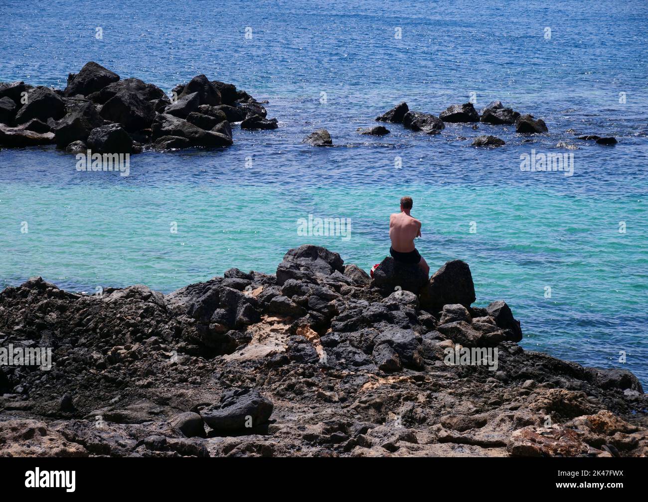 L'uomo si siede con la schiena su una roccia e guarda rilassato il mare Foto Stock