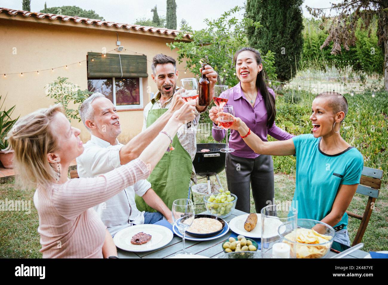 Tostare bicchieri da vino e birre con gli amici durante l'evento del fine settimana. Un gruppo di persone che bevono alcol nel cortile della casa in estate. Concetto di stile di vita. Foto Stock Tostare bicchieri da vino e birre con gli amici durante l'evento del fine settimana. Un gruppo di persone che bevono alcol nel cortile della casa in estate. Concetto di stile di vita. Foto Stock