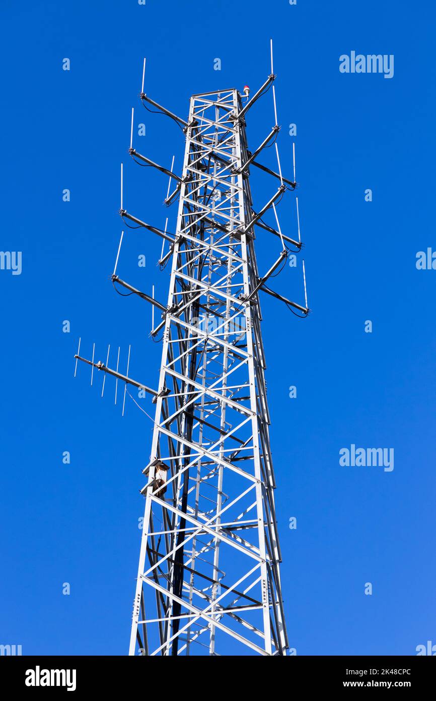 La torre di comunicazione bianca con i dispositivi radio è sotto il cielo blu in una giornata di sole Foto Stock