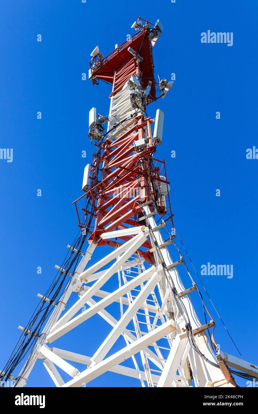 La torre di telecomunicazione bianca rossa con dispositivi radio è sotto il cielo blu in una giornata di sole Foto Stock