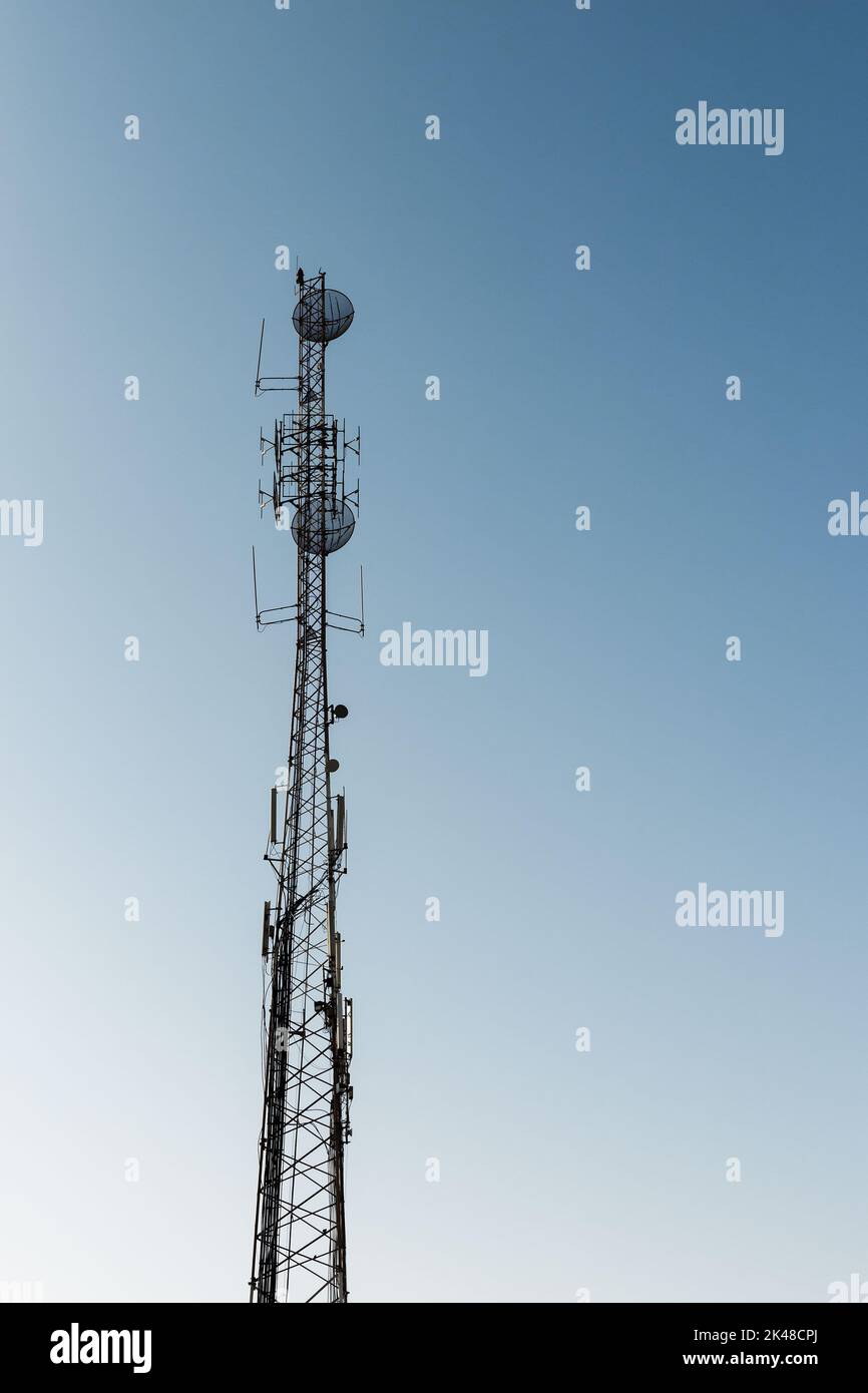 L'alta torre di telecomunicazione con dispositivi radio è sotto il cielo blu, foto di silhouette verticale Foto Stock