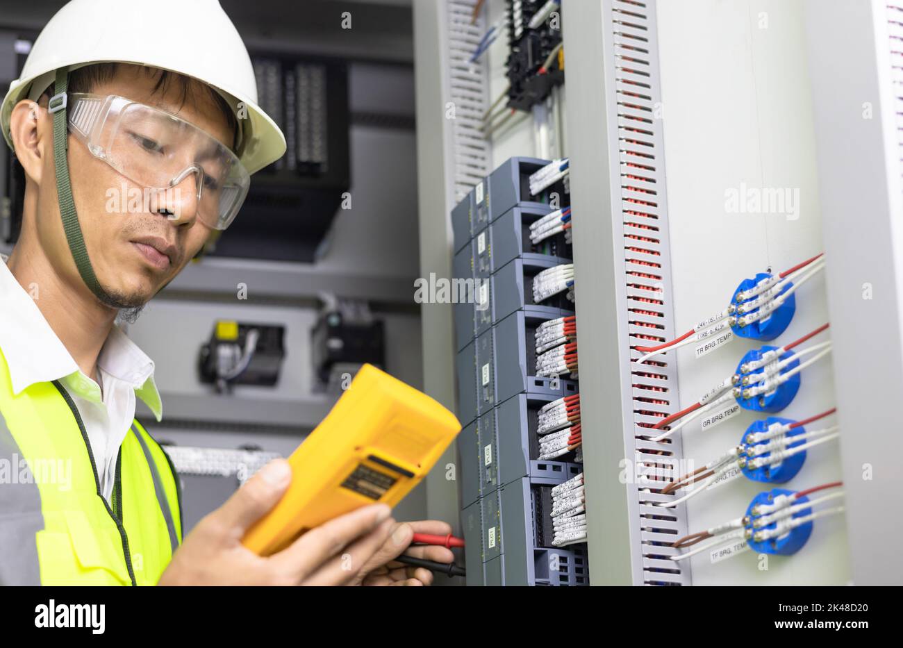 Un elettricista maschio lavora in un quadro elettrico, morsettiera elettrica. Pannello di controllo con contattore magnetico e relè di sovraccarico, misurazione della tensione in ma Foto Stock