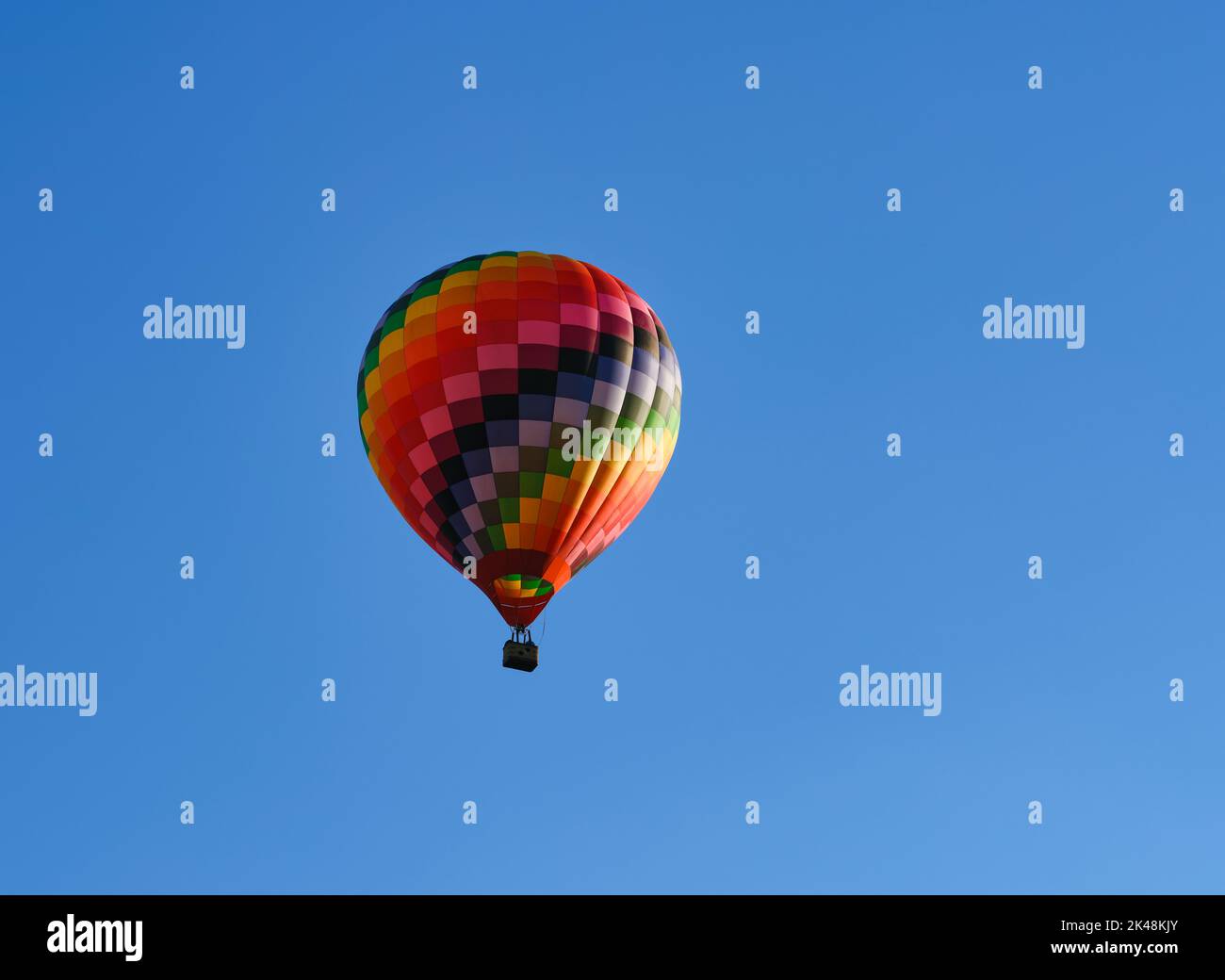 Palloncino colorato ad aria calda che vola attraverso il cielo blu. Foto Stock