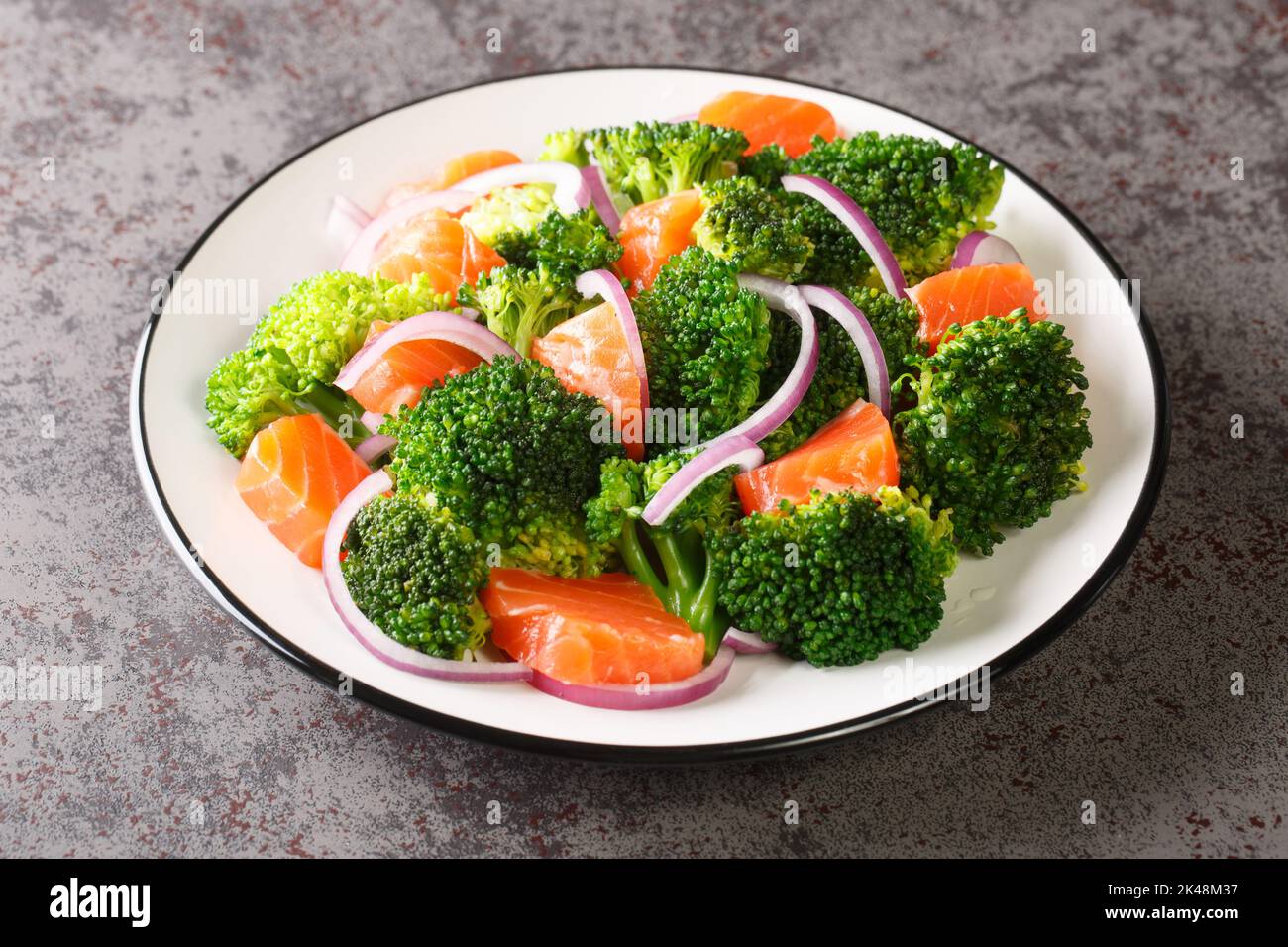 Insalata di vitamine di broccoli al vapore, salmone salato e cipolla rossa fresca condita con olio d'oliva primo piano in un piatto sul tavolo. Orizzontale Foto Stock