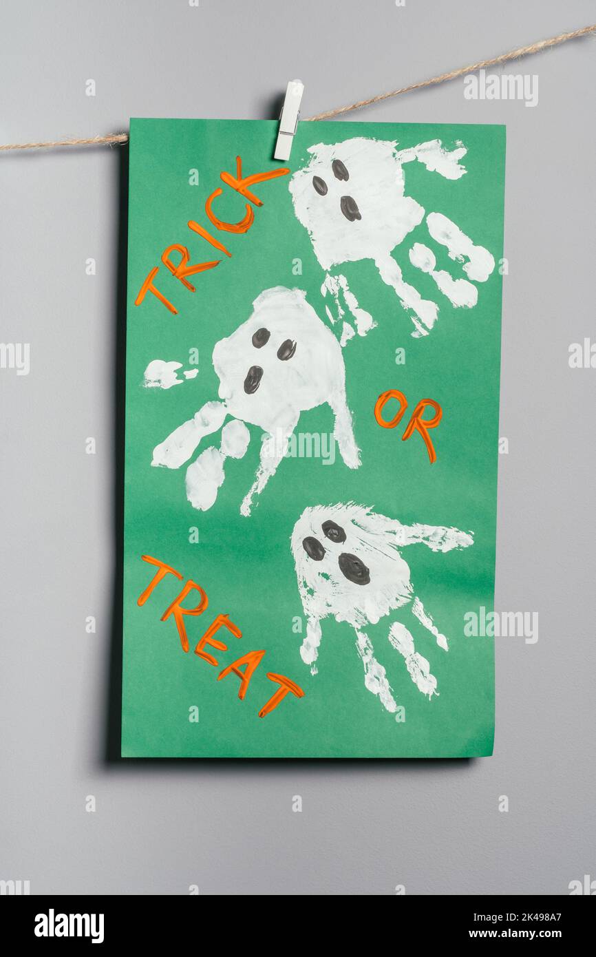 Halloween fantasmi bianchi peperoncini disegni su carta verde appeso su corda sulla parete grigia. Decorazioni fai da te fatte a mano con bambini per le vacanze Foto Stock