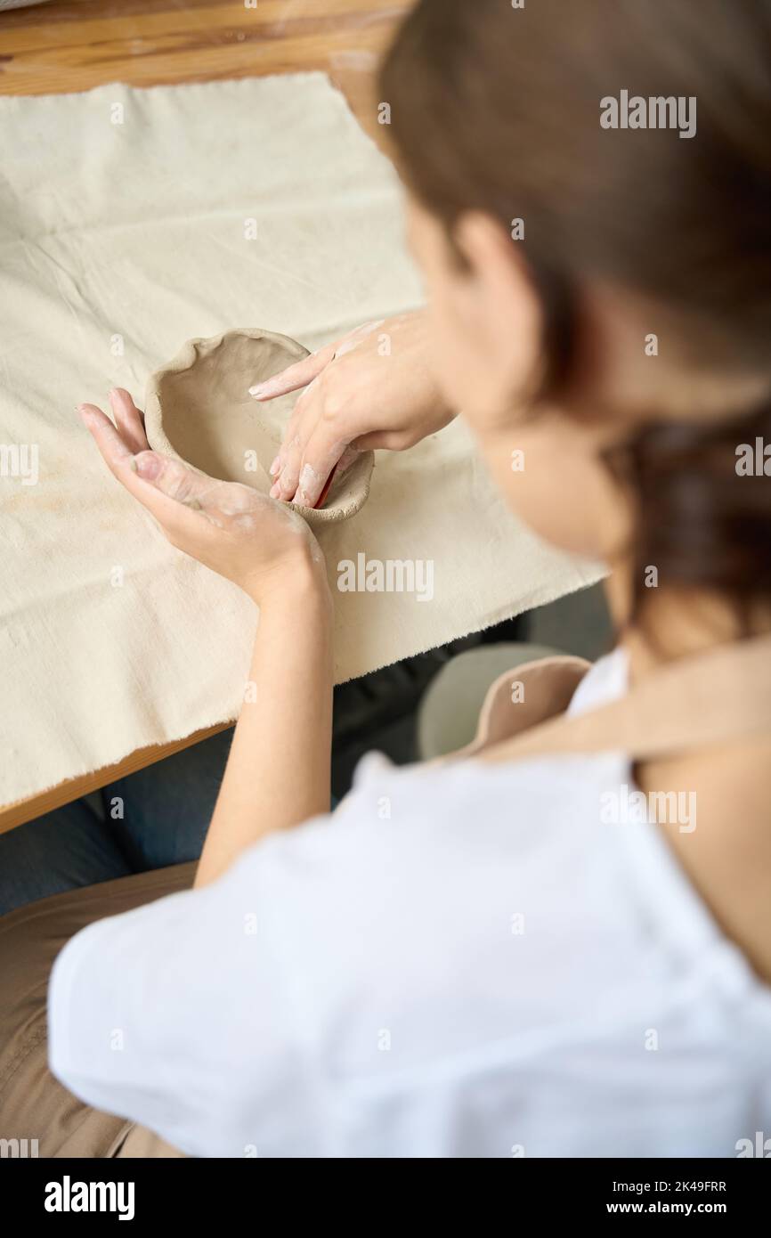 Donna siede tavolo di legno e scolpisce un piatto di argilla Foto Stock