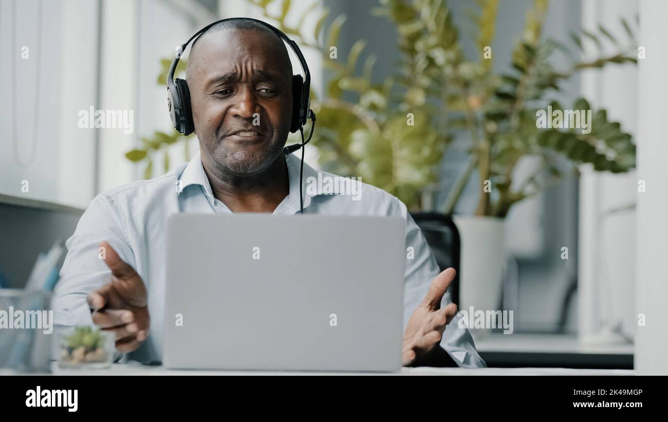 L'insegnante africano senior dell'istruttore indossa le cuffie usando la macchina fotografica di fotoricettore per la comunicazione con i clienti che insegnano la video consultazione in linea durante Foto Stock