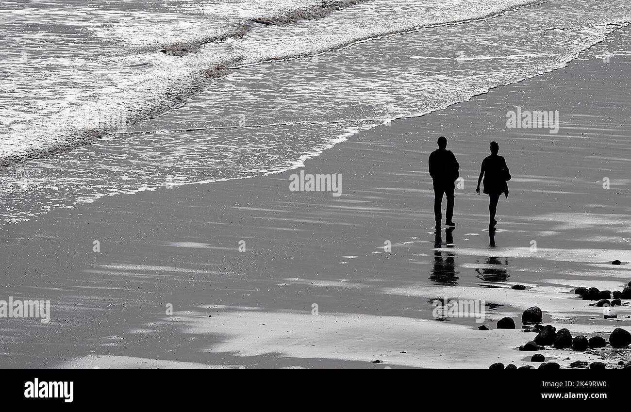 Persone in silhouette camminando sulla spiaggia bagnata. Foto Stock