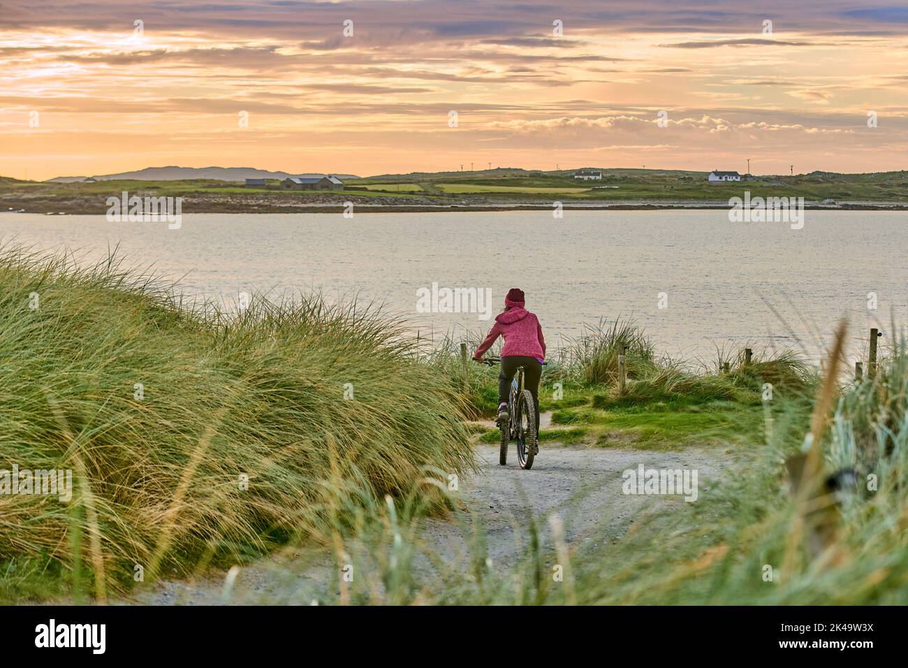 Bella donna anziana in mountain bike, in bicicletta al tramonto sulla spiaggia di sabbia dorata di Sillerna, Grallagh, County Galway, nella parte occidentale della Repubblica Foto Stock