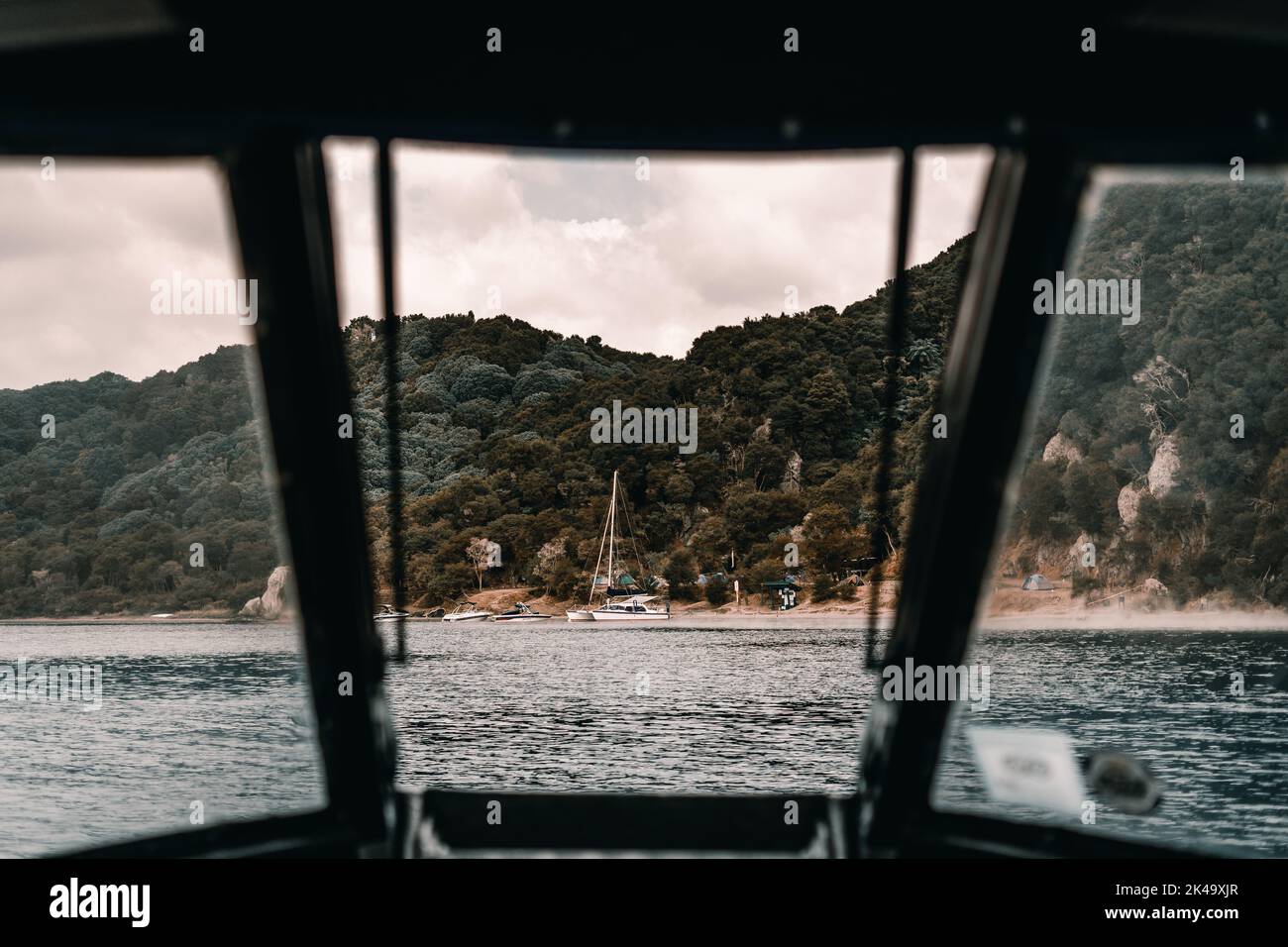 vista della spiaggia del catamarano e della lussureggiante foresta dall'interno di una barca che naviga sul lago arrivando a riva, il lago tarawera, nuova zelanda Foto Stock