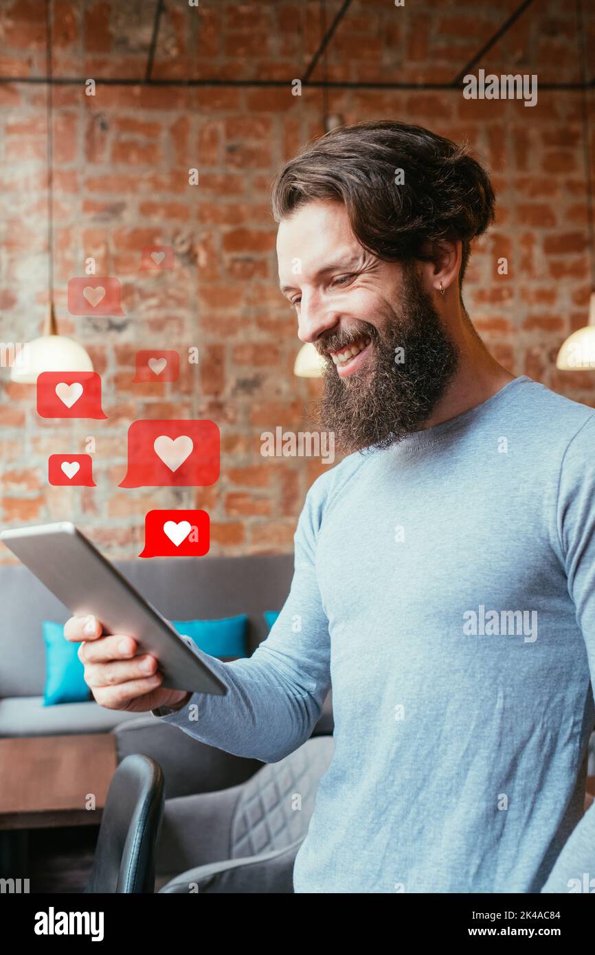 Come i social media. Feedback positivo. Comunicazione globale online. Sorridente hipster blogger maschio utilizzando tablet con icone del cuore illustrazione in loft int Foto Stock