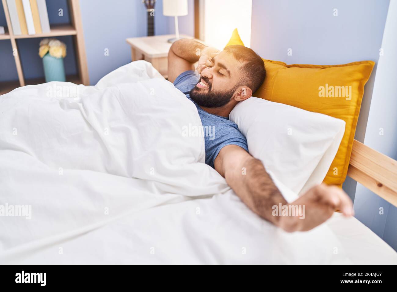 Giovane ispanico che si svegliò stendendo le braccia in camera da letto Foto Stock