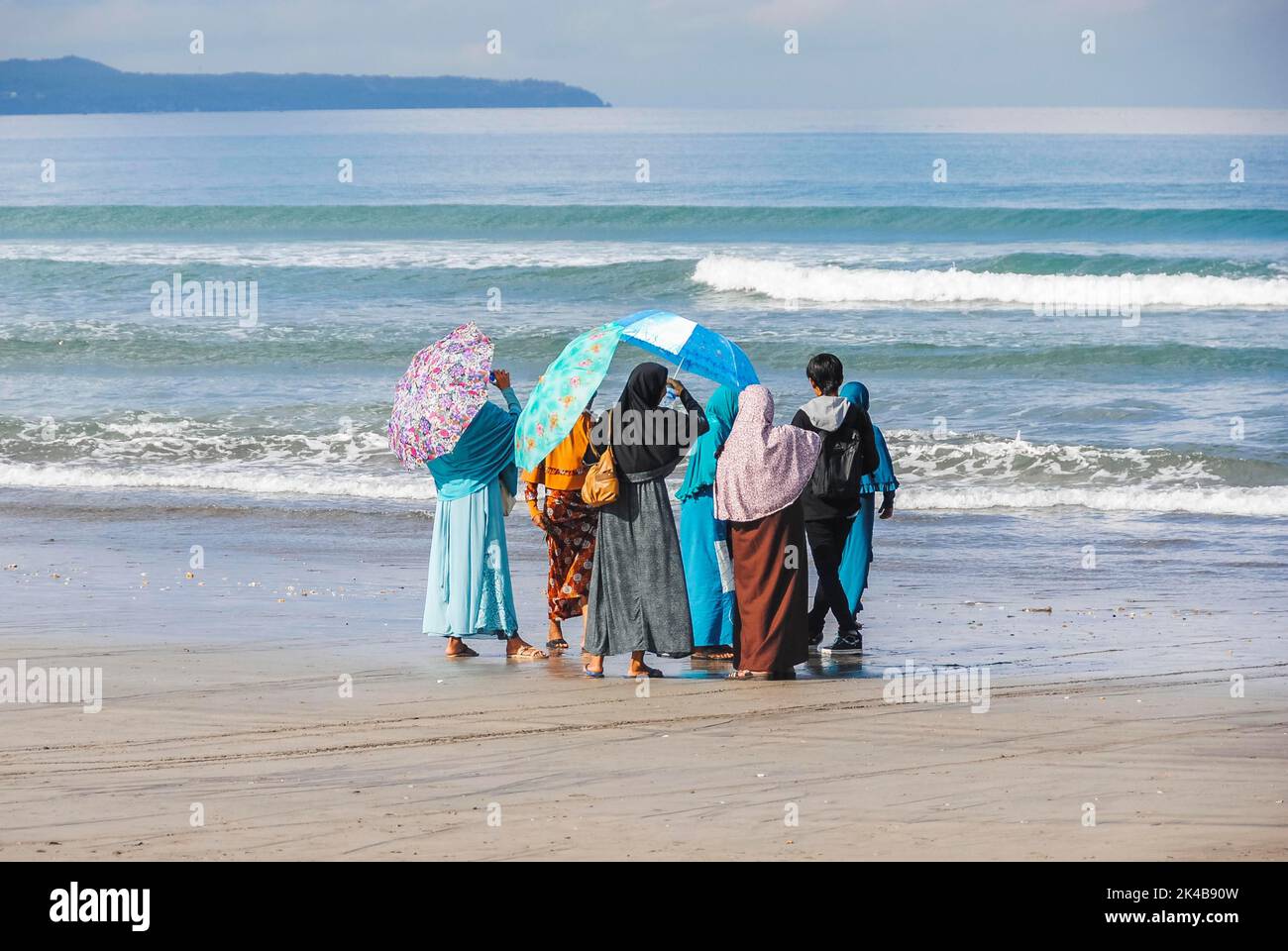 Donne musulmane e un giovane uomo che guarda verso il mare sulla spiaggia di Bali, Indonesia Foto Stock