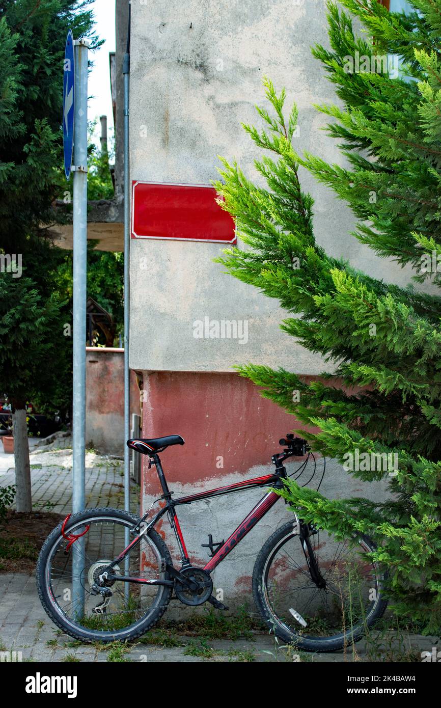 Bicicletta appoggiata al muro sulla strada. Area postale vuota sul cartello rosso della parete. Foto Stock