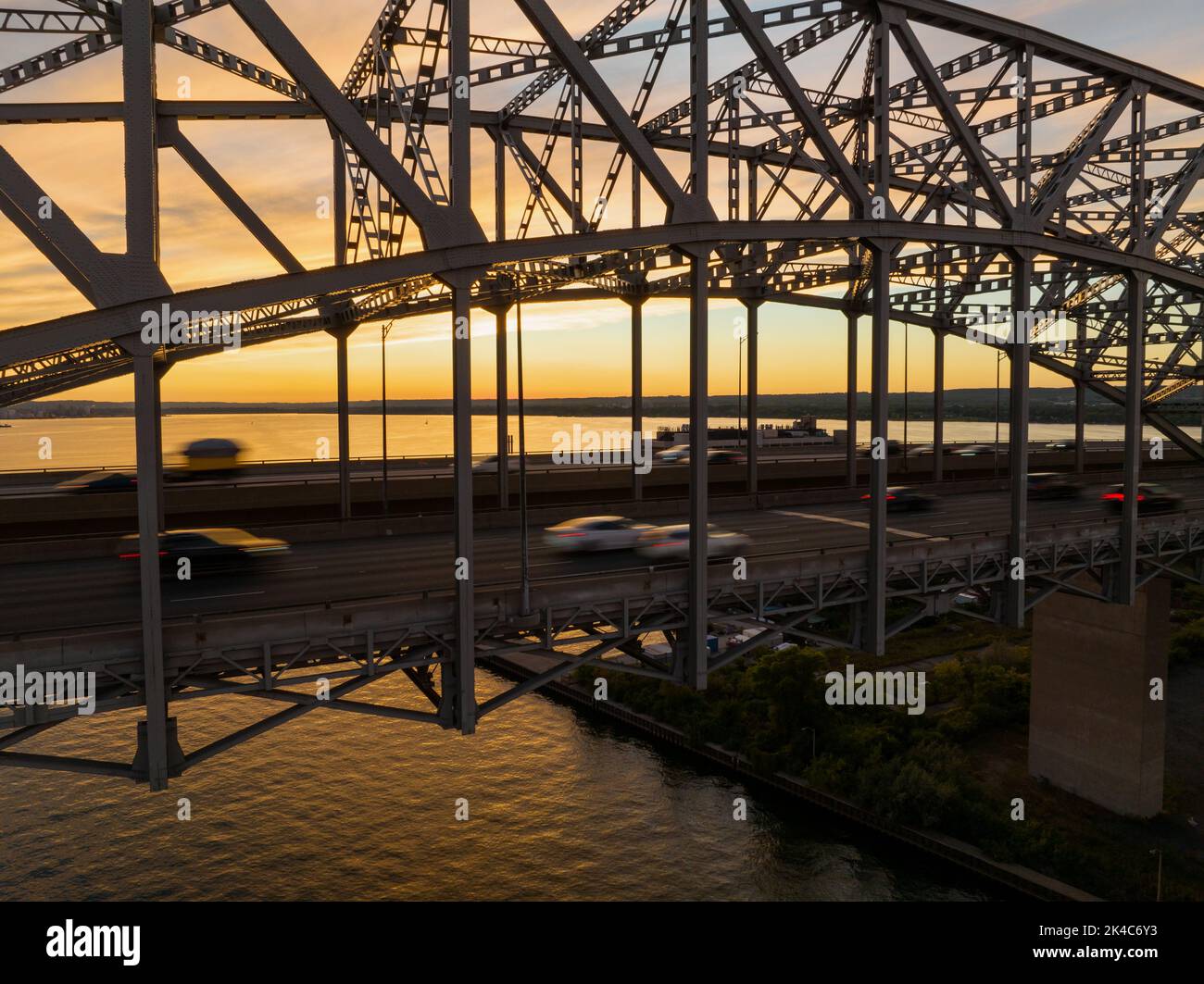 Un grande ponte a capriate su un vasto corpo d'acqua è visto al tramonto come auto, movimento sfocato, viaggiare attraverso l'autostrada a più corsie. Foto Stock