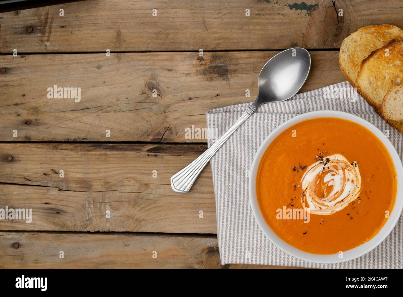 Immagine orizzontale della ciotola di zuppa di pomodoro con cucchiaio e pane tostato su legno, spazio copia Foto Stock