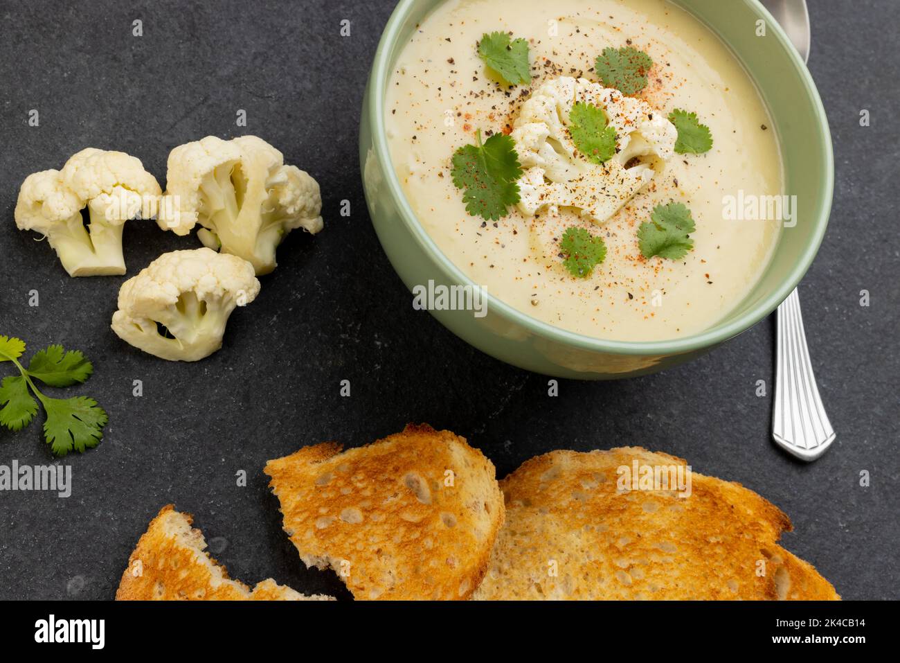 Immagine orizzontale della zuppa di cavolfiore con contorno, con pane tostato e fiori su ardesia Foto Stock