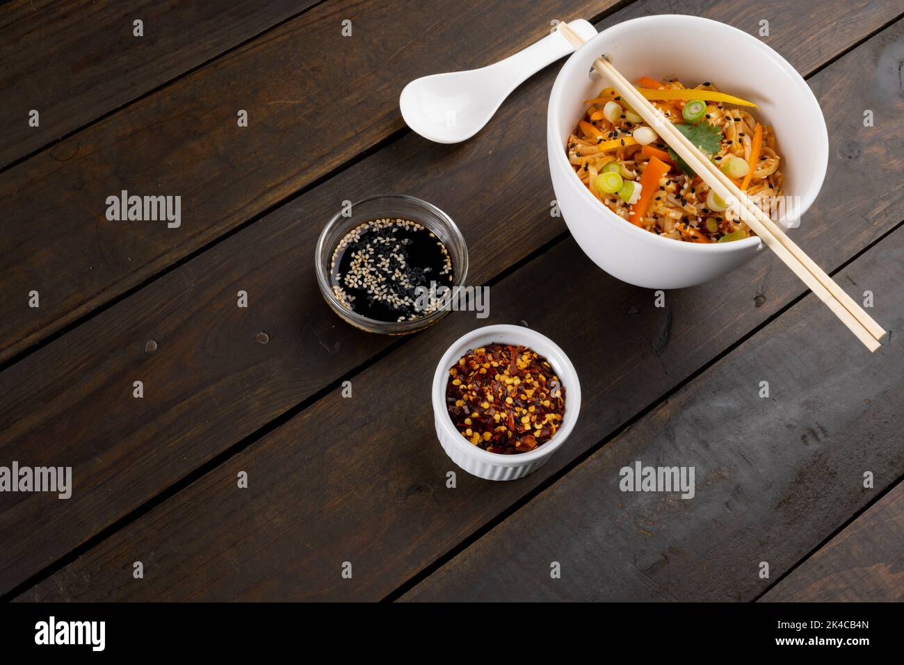 Il wok asiatico soffrigna spaghetti e bacchette e condimenti su sfondo di legno Foto Stock