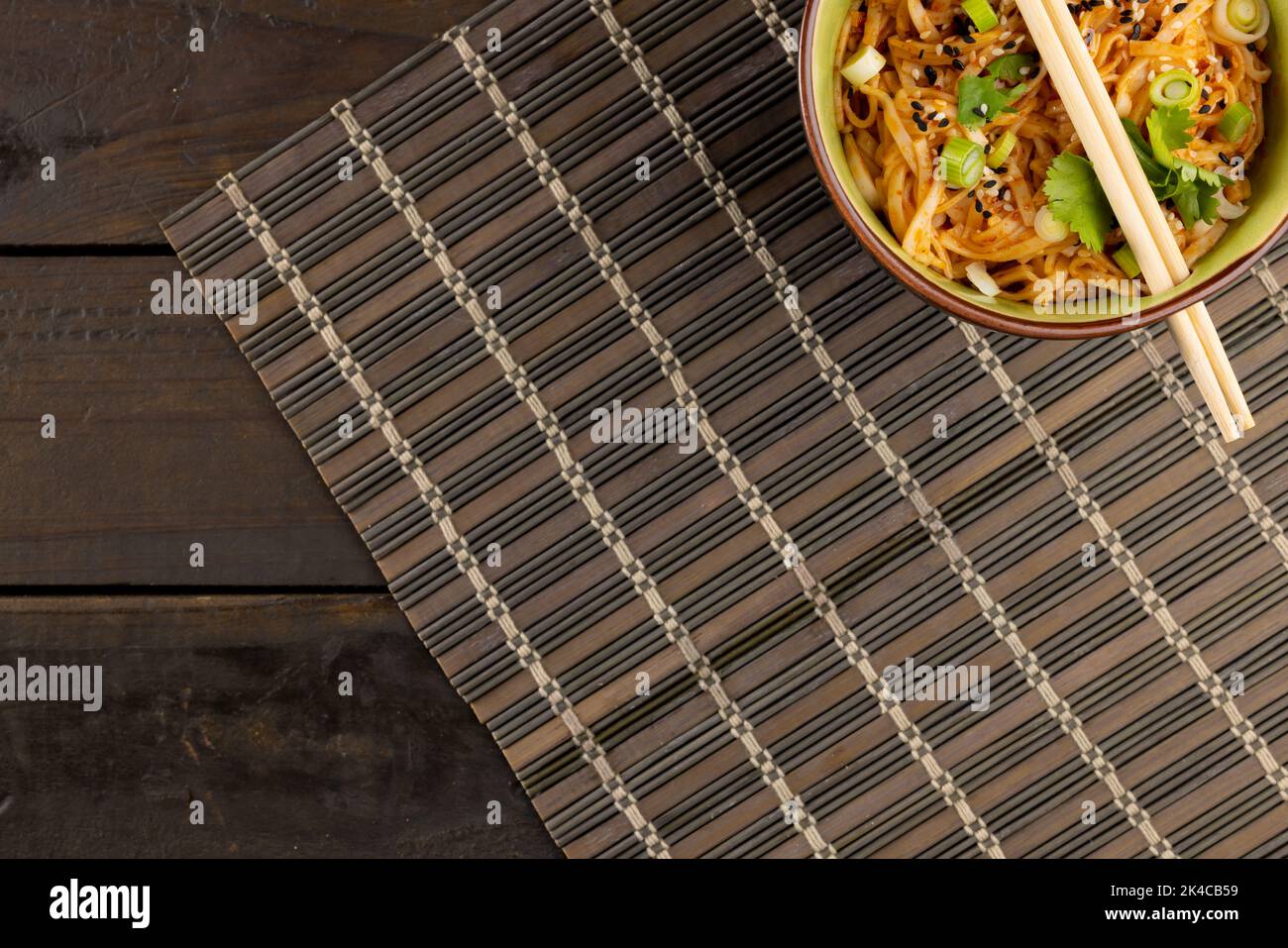 Vista dall'alto del wok asiatico, spaghetti saltati con bacchette sul tappeto e tavole di legno Foto Stock