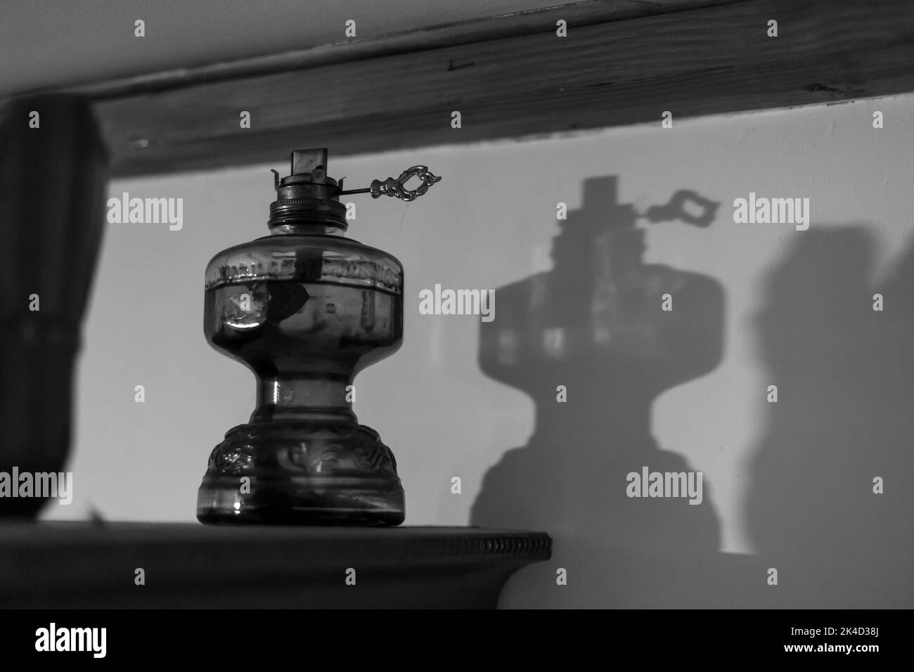 Una foto in scala di grigi di una vecchia lampada a lanterna sporca in una stanza con la sua silhouette sulla parete Foto Stock