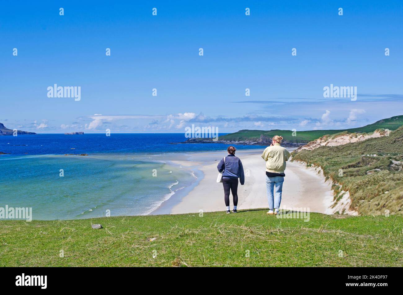 Giovani coppie guardano fuori sulla bella spiaggia vuota all'estremità della baia di Balnakeil, di Durness, Sutherland, con il promontorio erboso di Faraid Head sulla destra. Foto Stock