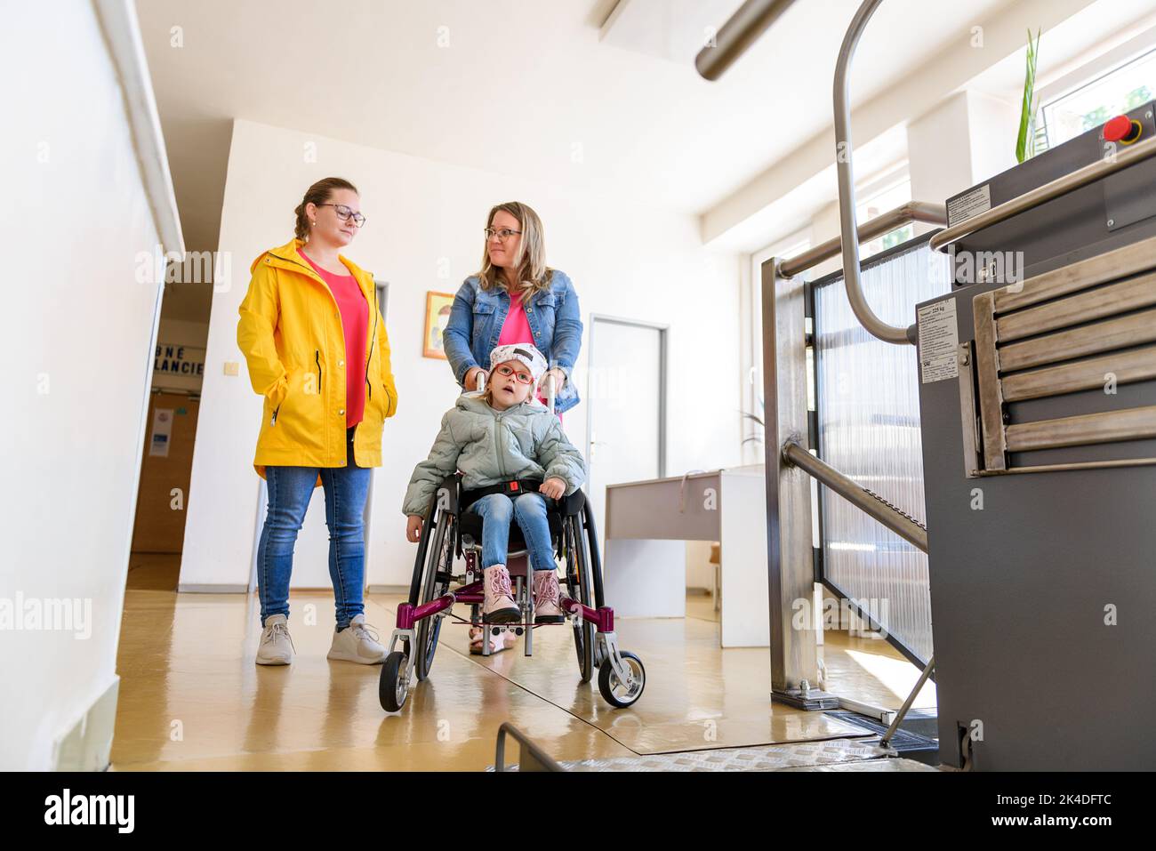 Madre con un bambino che vive con paralisi cerebrale utilizzando un ascensore elettrico per sedie a rotelle per accedere all'edificio pubblico. Speciale piattaforma di sollevamento per sedia a rotelle Foto Stock