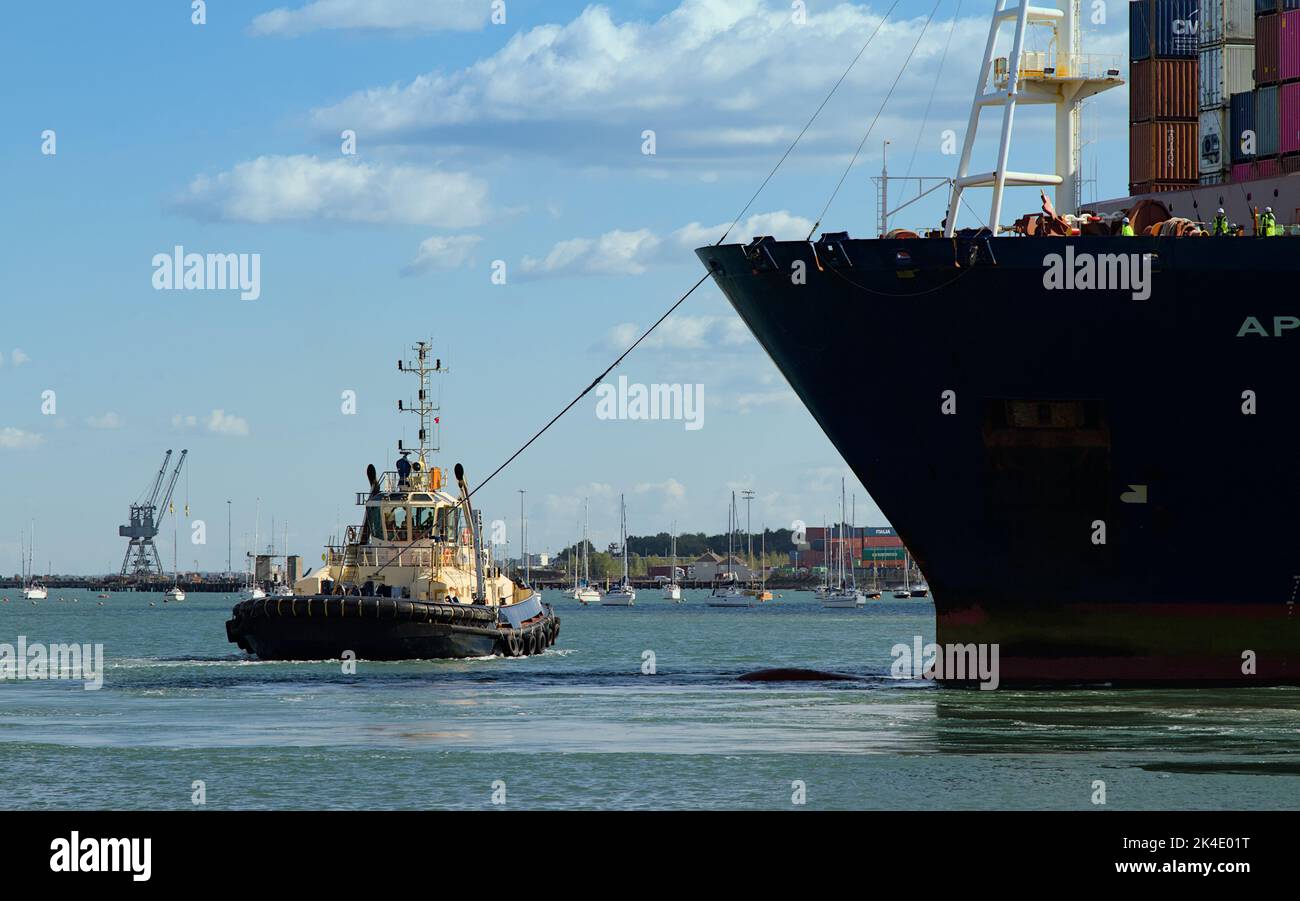 Rimorchiatore che tira Una grande nave container con Una Tow Line nel porto di Southampton Docks UK Foto Stock