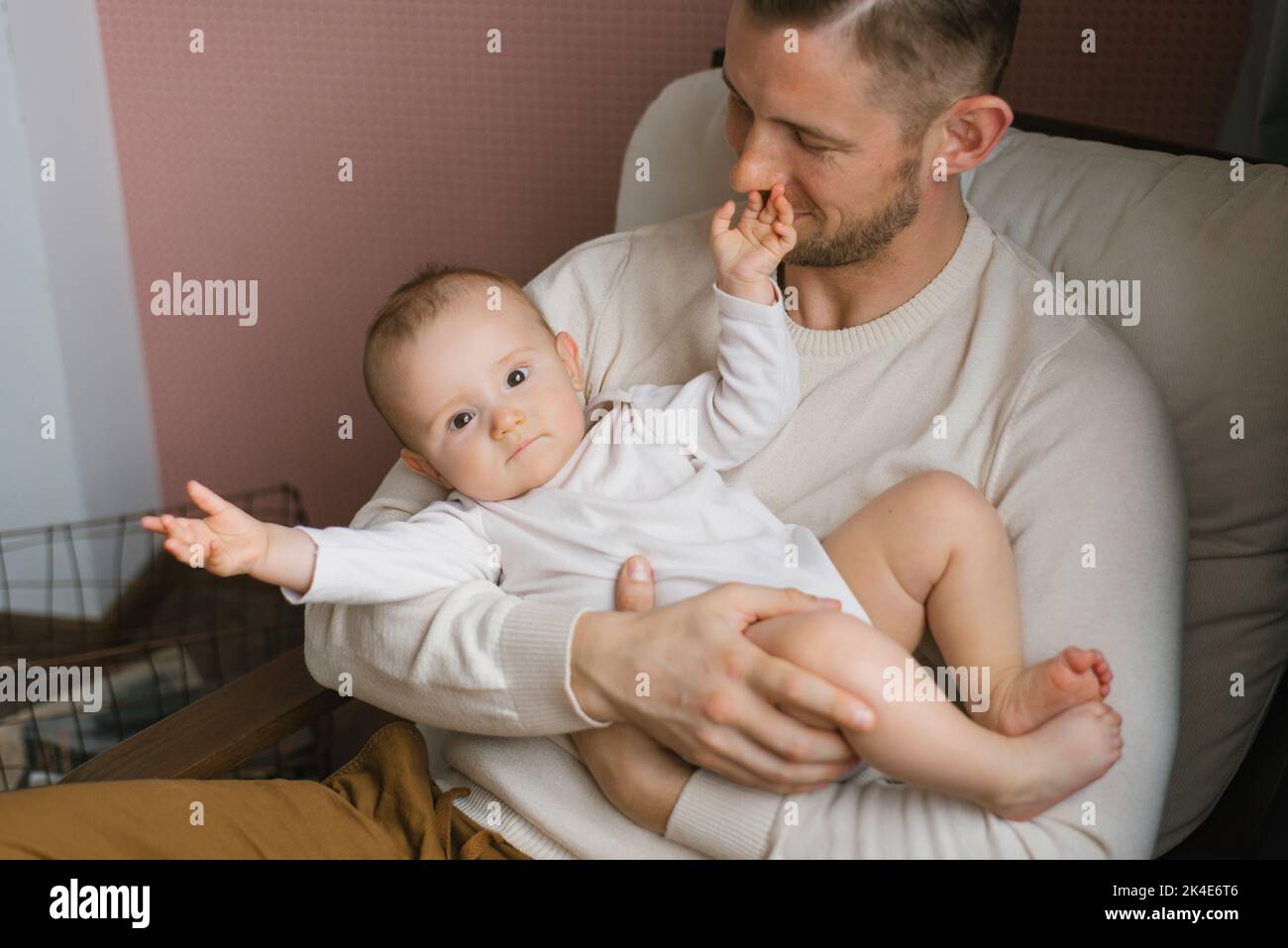 Un felice padre contenta tiene il figlio del bambino fra le braccia e si siede a casa in una poltrona Foto Stock