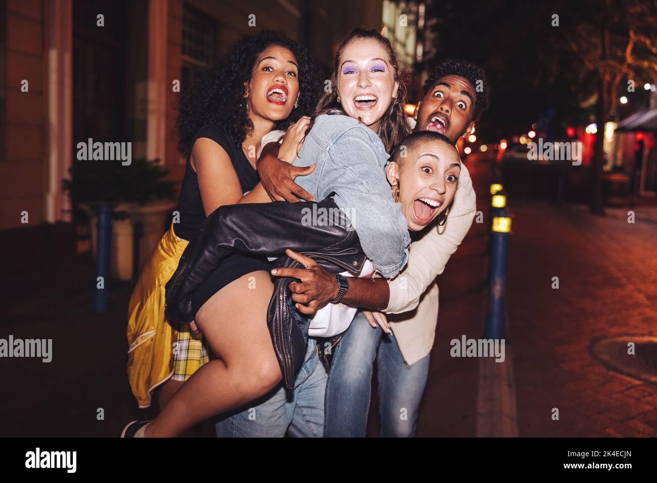 Amici pazzi che si divertono insieme in città. Giovani multiculturali che urlano felicemente mentre si appendono insieme all'aperto di notte. Gruppo di frie Foto Stock