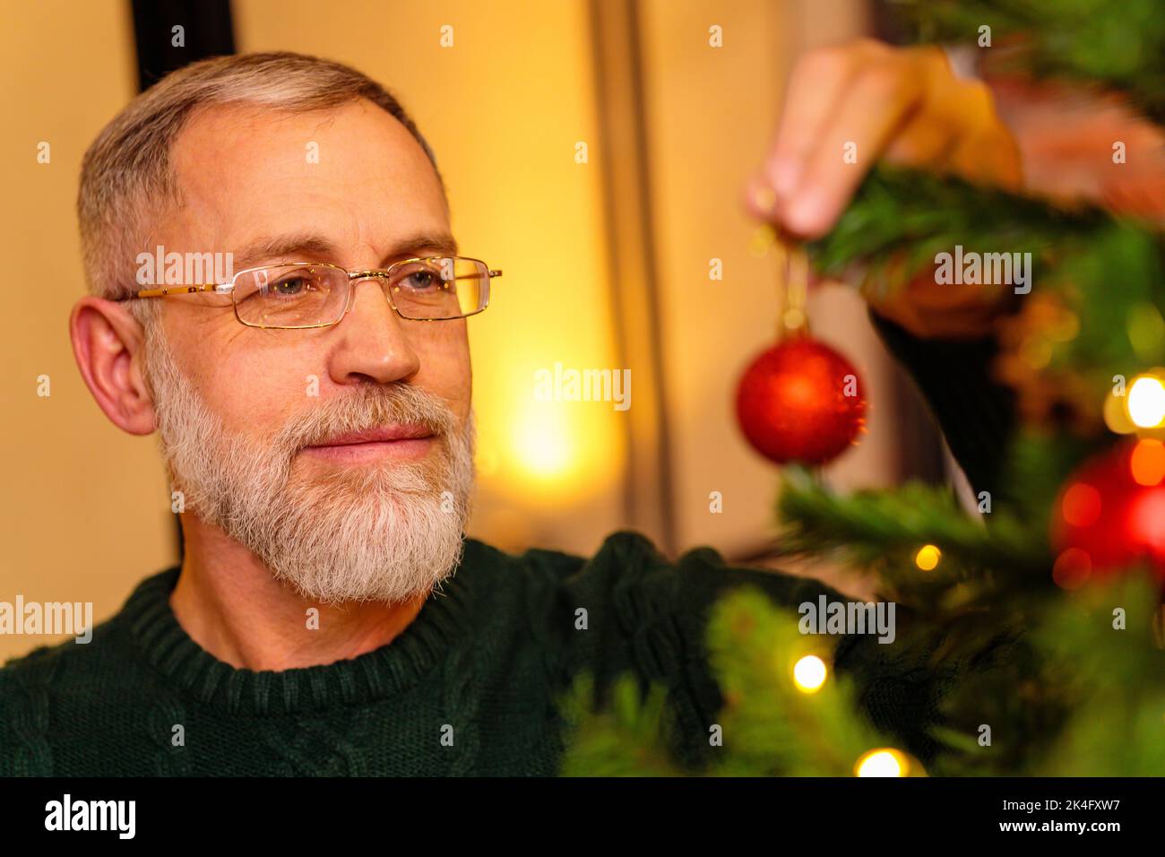 Un uomo anziano in una maglia verde che decora l'albero di Natale Foto Stock
