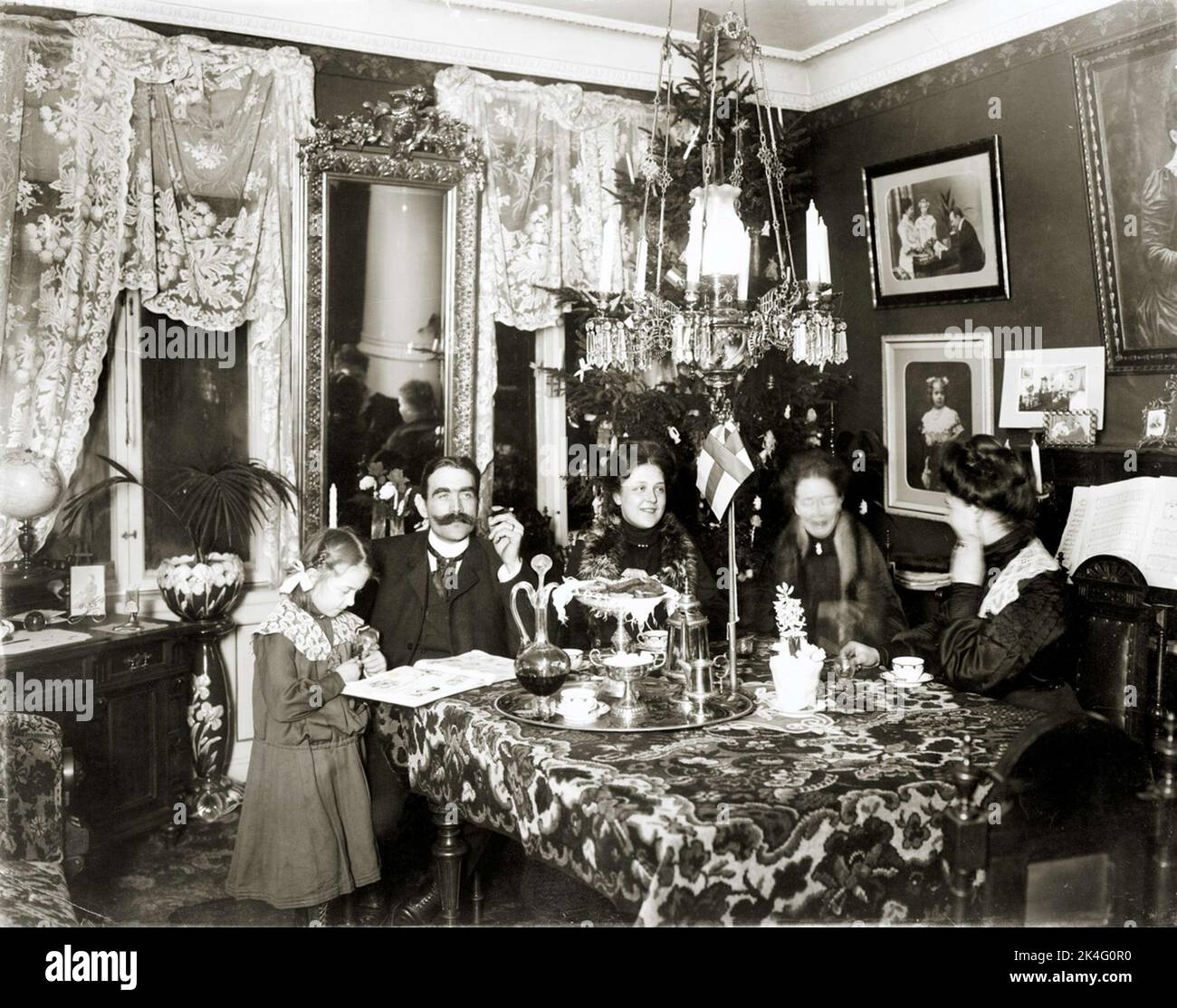 Celebrazione di Natale, ambiente casa borghese intorno alla fine del secolo 1900. Caffè per tutta la famiglia nel salone. Bandiera dell'Unione in miniatura sul tavolo. Nordico Foto Stock