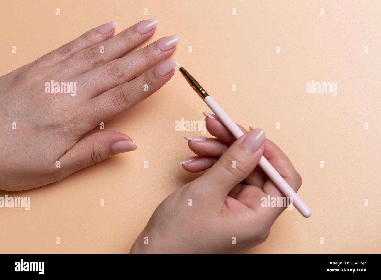 Chiodo per pittura con piccola spazzola sulle mani di donna in colore beige fondo Foto Stock