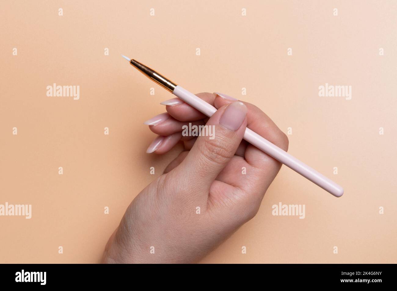 Piccola spazzola cosmetica in mano donna vista primo piano su sfondo di colore beige Foto Stock