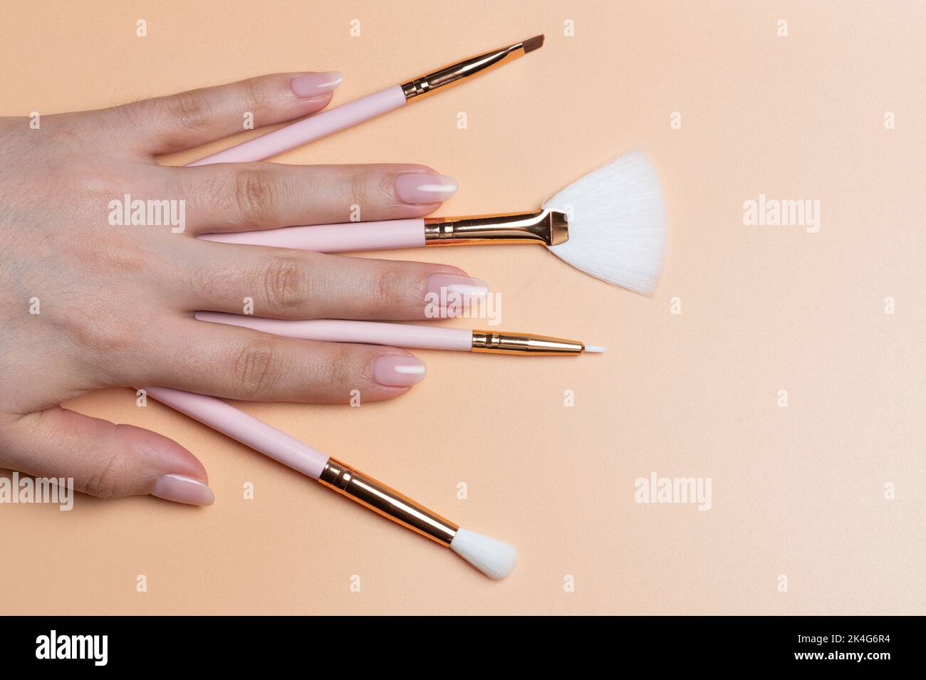 Molti pennelli di make up diversi in mano donna vista ravvicinata su sfondo di colore beige Foto Stock