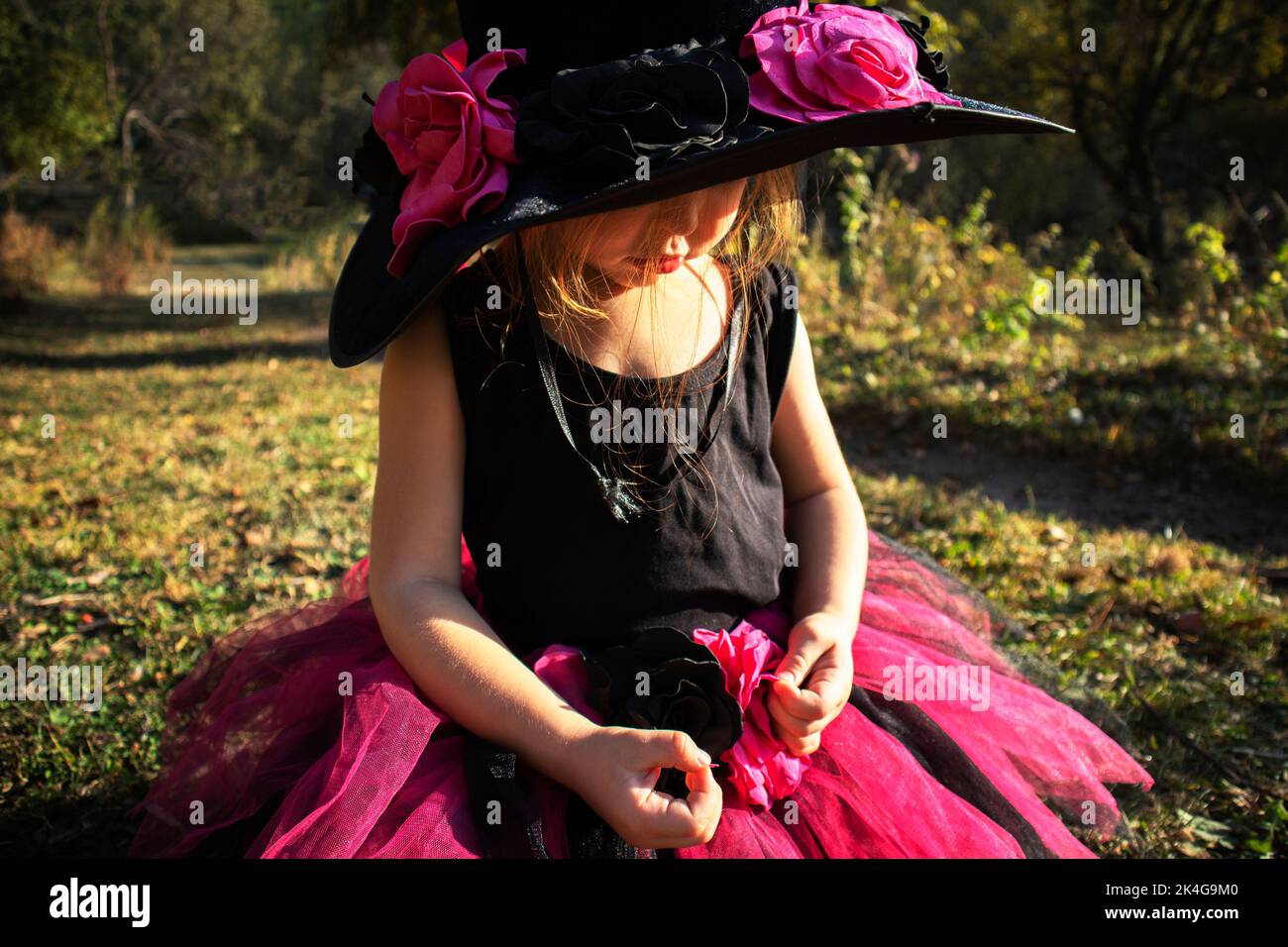 una bambina in costume da strega si siede e guarda giù Foto Stock