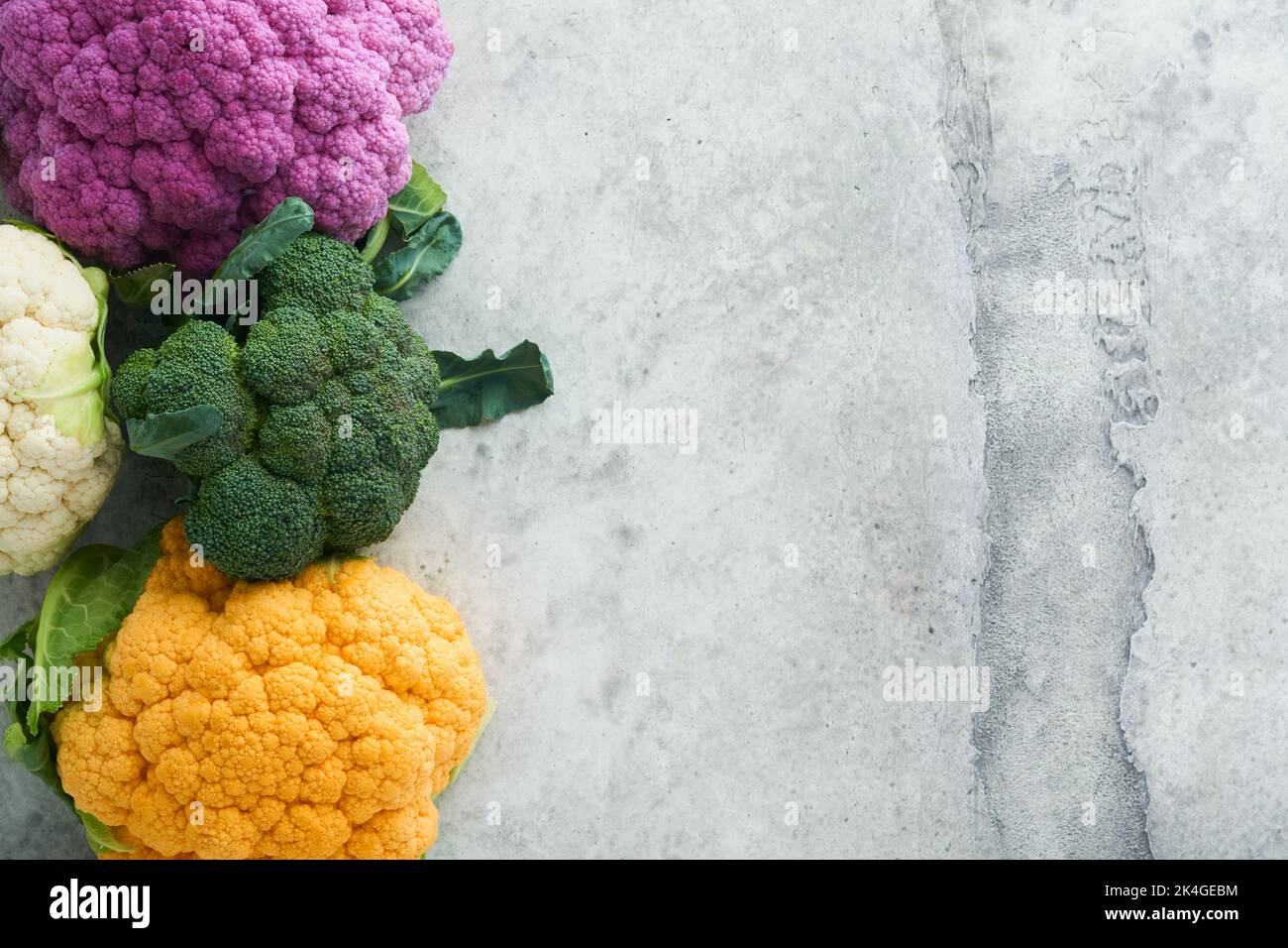 Cavolfiore di Colorfu. Vari tipi di cavolfiore su fondo grigio in cemento. Cavoli di colore viola, giallo, bianco e verde. Broccoli e Romanesco. Foto Stock