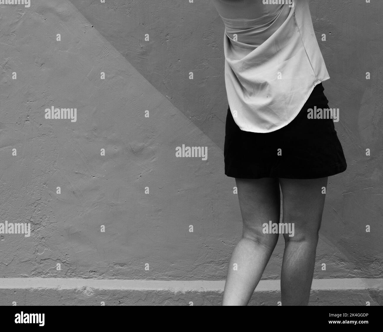 Un bianco e nero delle gambe della donna in una breve gonna nera davanti ad una parete. Foto Stock