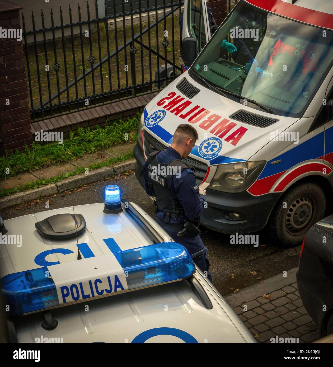 Una polizia europea in uniforme che utilizza un cellulare in servizio davanti alla macchina della polizia accanto a un'ambulanza. Scena del crimine e concetto di indagine Foto Stock