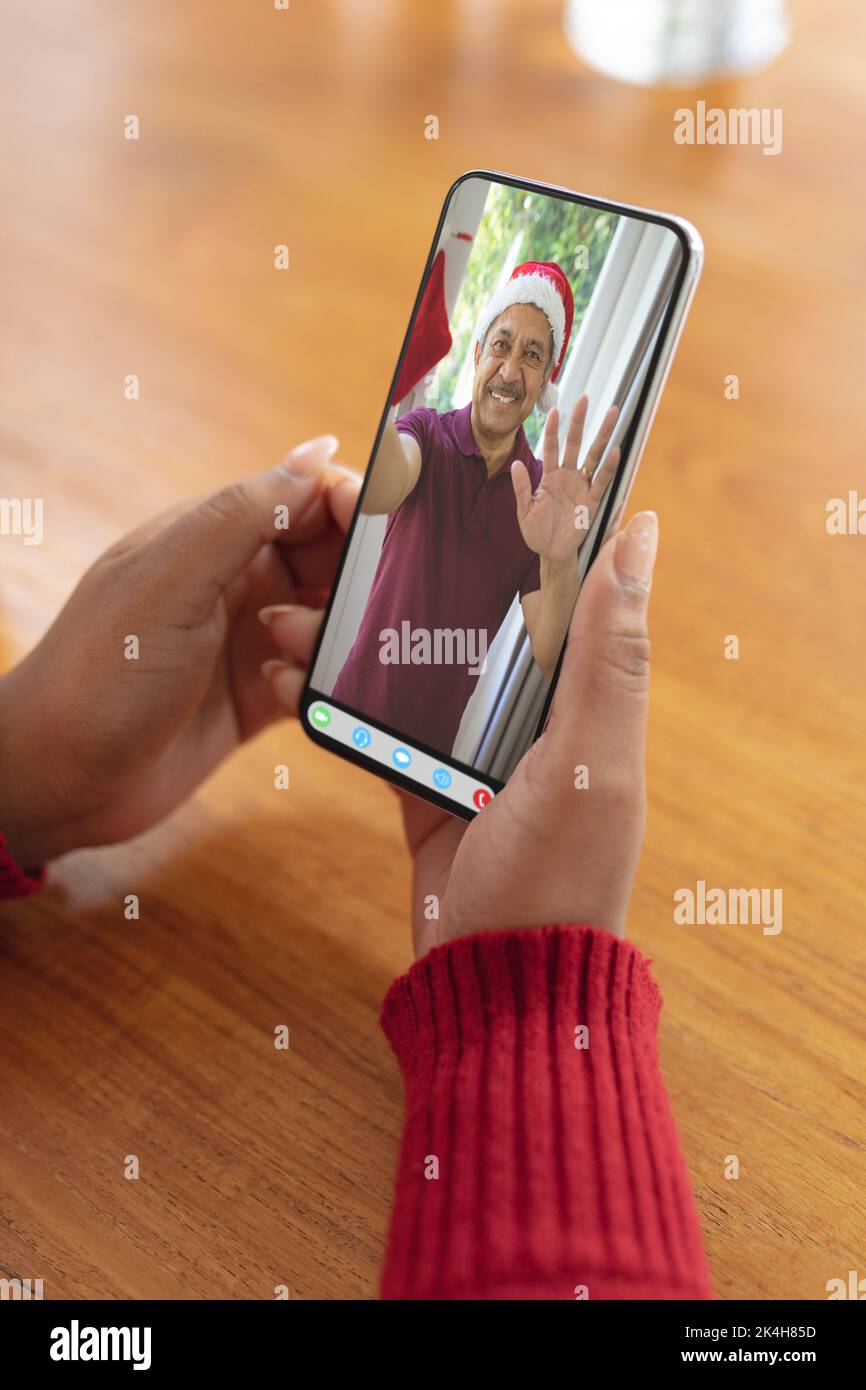 Le mani di una donna che effettua una videochiamata natalizia con un uomo biraciale anziano sorridente a santa Hat. natale, festa e tecnologia di comunicazione Foto Stock