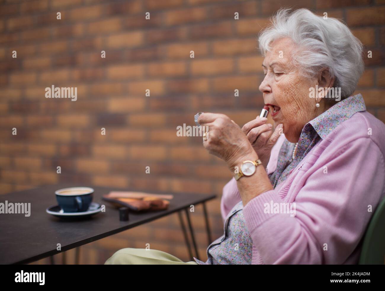 Donna anziana felice che mette il rossetto sulle sue labbra godendosi il caffè in città. Foto Stock