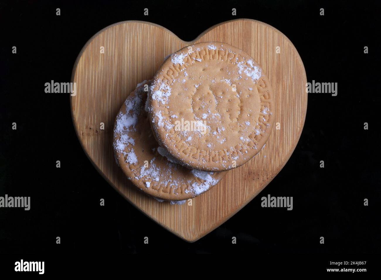 Delizia turca all'interno biscotti su un cuore di legno su uno sfondo nero con zucchero alimentato. Foto Stock
