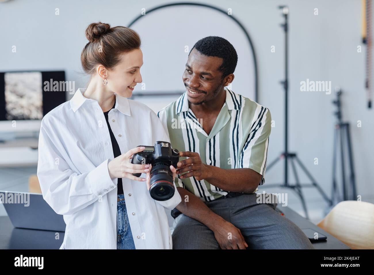 Ritratto minimale in vita di due giovani fotografi che guardano le immagini in fotocamera e sorridono Foto Stock