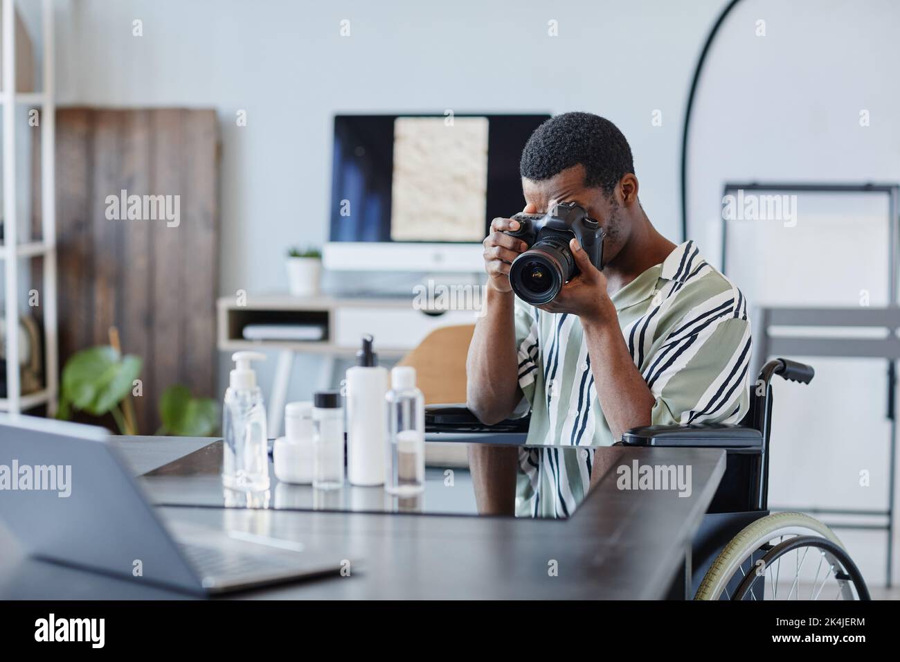 Ritratto di un giovane uomo nero come fotografo con disabilità che scatta foto di prodotti in studio fotografico Foto Stock