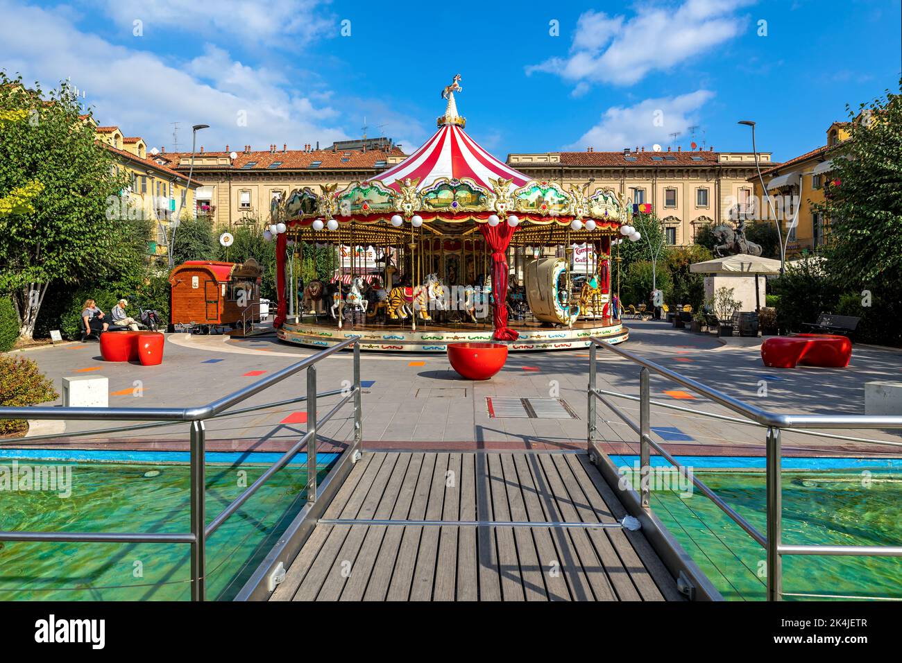 Carosello colorato su piccola piazza con fontana moderna ad Alba - città in Piemonte, Italia settentrionale. Foto Stock