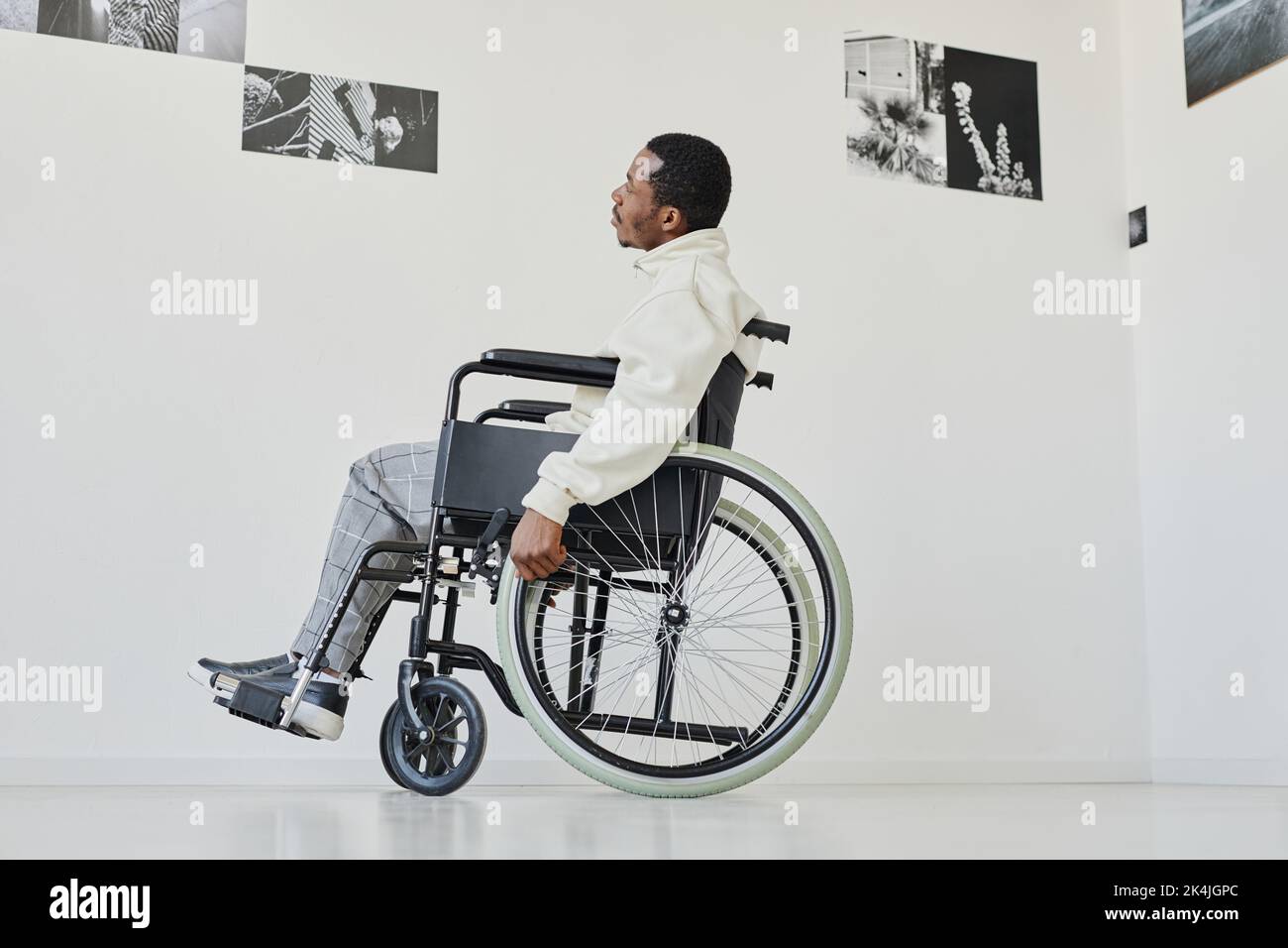 Ritratto con vista laterale di un giovane uomo nero su sedia a rotelle mentre si visita la galleria d'arte moderna, spazio copia Foto Stock