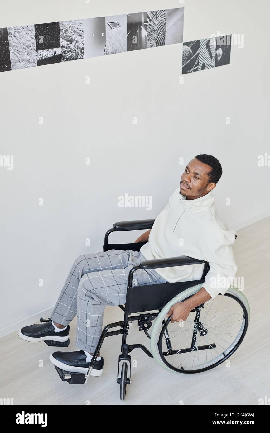 Ritratto ad angolo alto dell'uomo nero su sedia a rotelle mentre si visita la galleria d'arte moderna in bianco Foto Stock