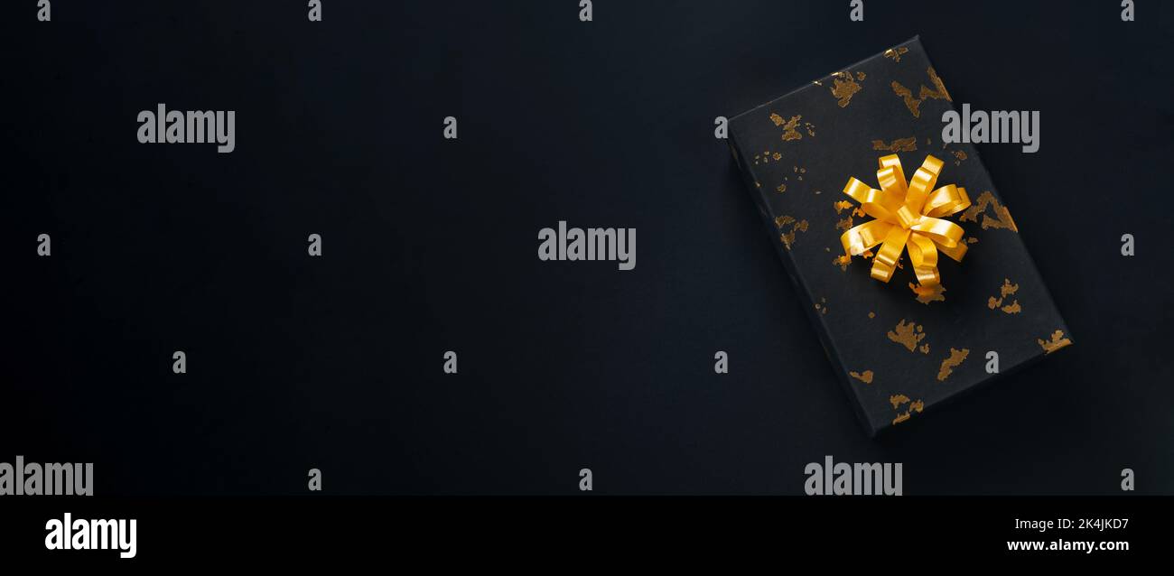 Nero presente con arco dorato su sfondo scuro. Concetto di Black friday o Christmas Holidays con spazio per le copie. Banner lungo Foto Stock