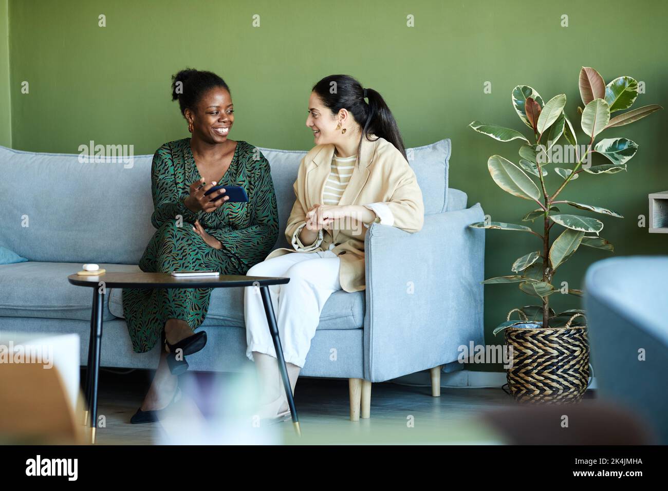 Due giovani donne d'affari interculturali che discutono qualcosa in smartphone tenuto da felice afro-americana dipendente femminile Foto Stock